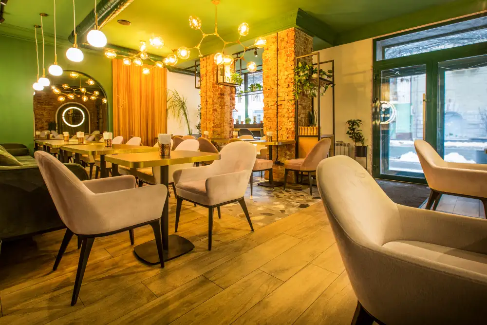 Einladender Gastraum eines modernen Bistros mit Tischen, Samtsesseln und Backsteinwand, fördert die Gemütlichkeit und Impulskäufe durch subtile Kaffeearomen.